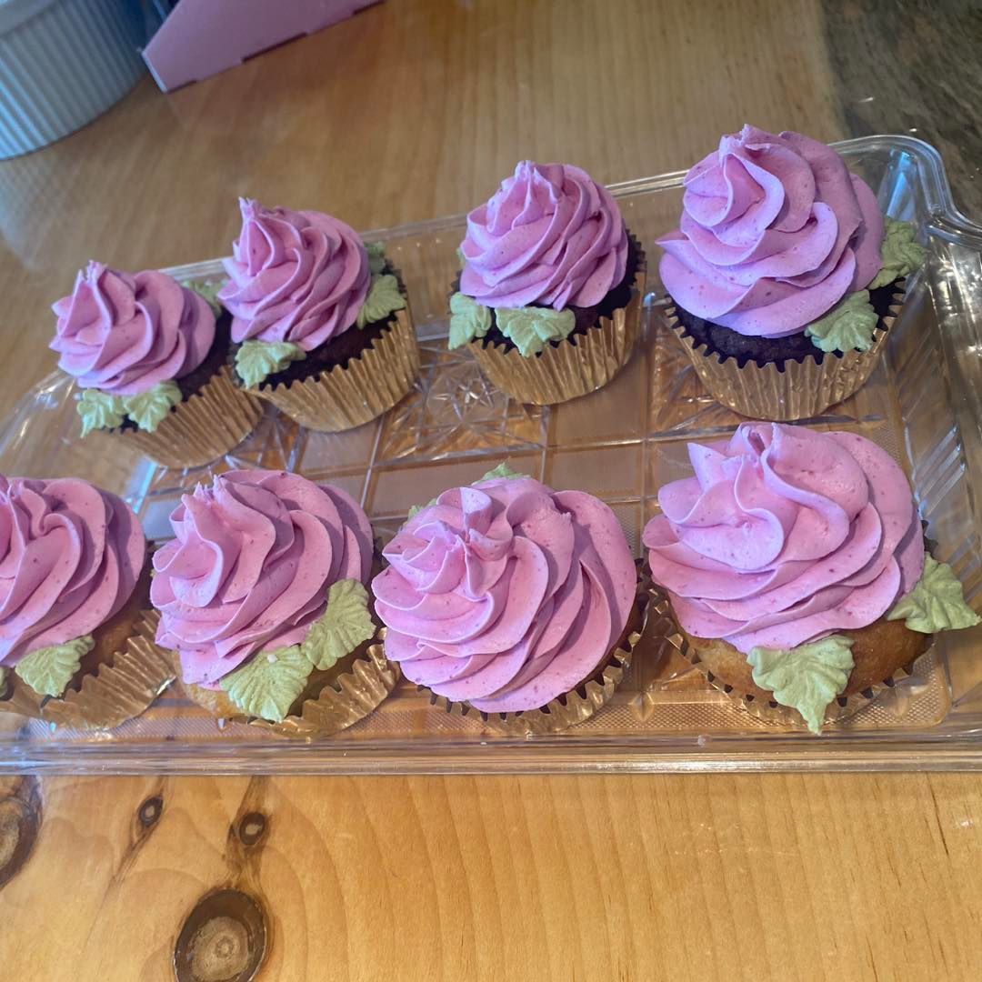 A tray of cupcakes with purple frosting on a wooden table