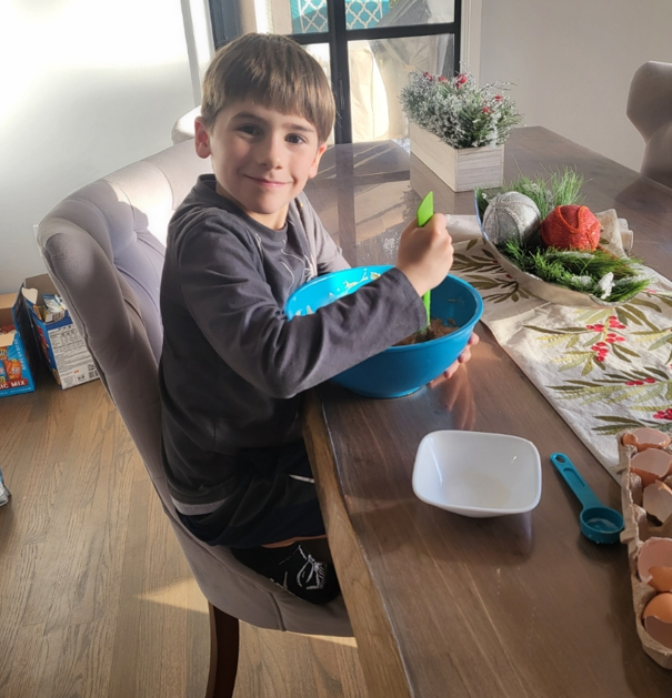 A young boy is sitting at a table holding a bowl of food