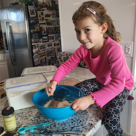 A little girl in a pink shirt is mixing something in a blue bowl