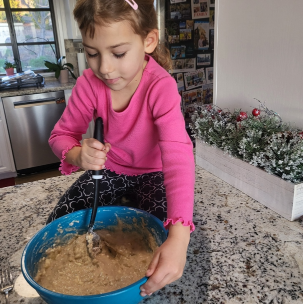 A little girl in a pink shirt is mixing something in a blue bowl