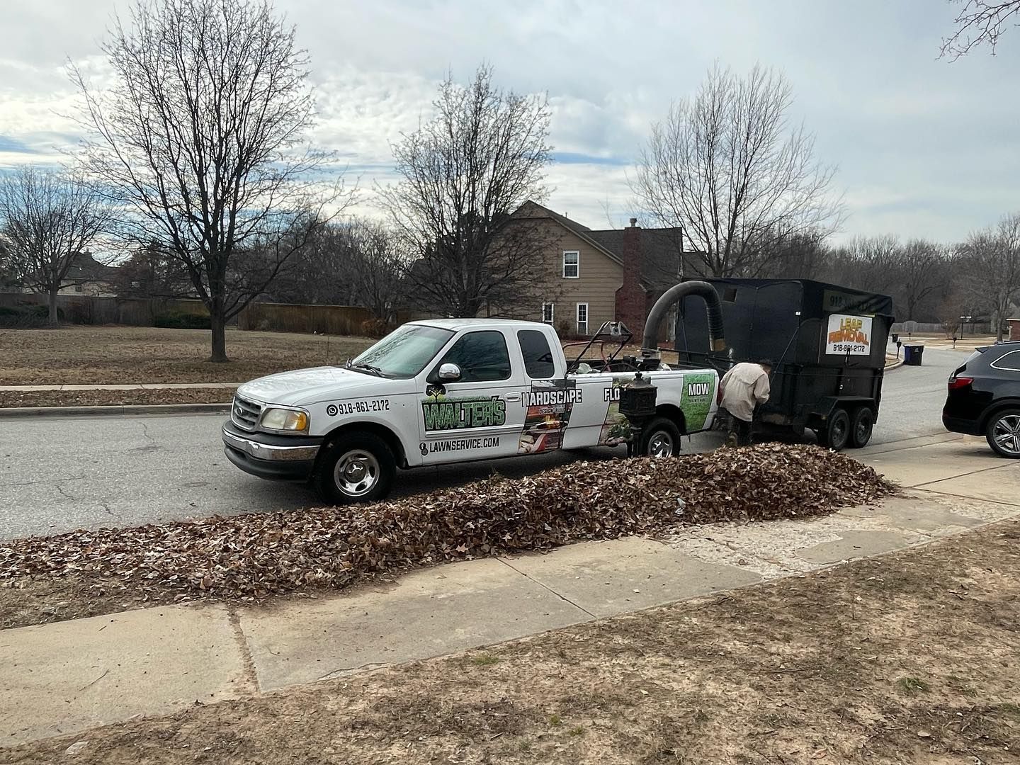 A white truck is parked on the side of the road next to a pile of leaves.