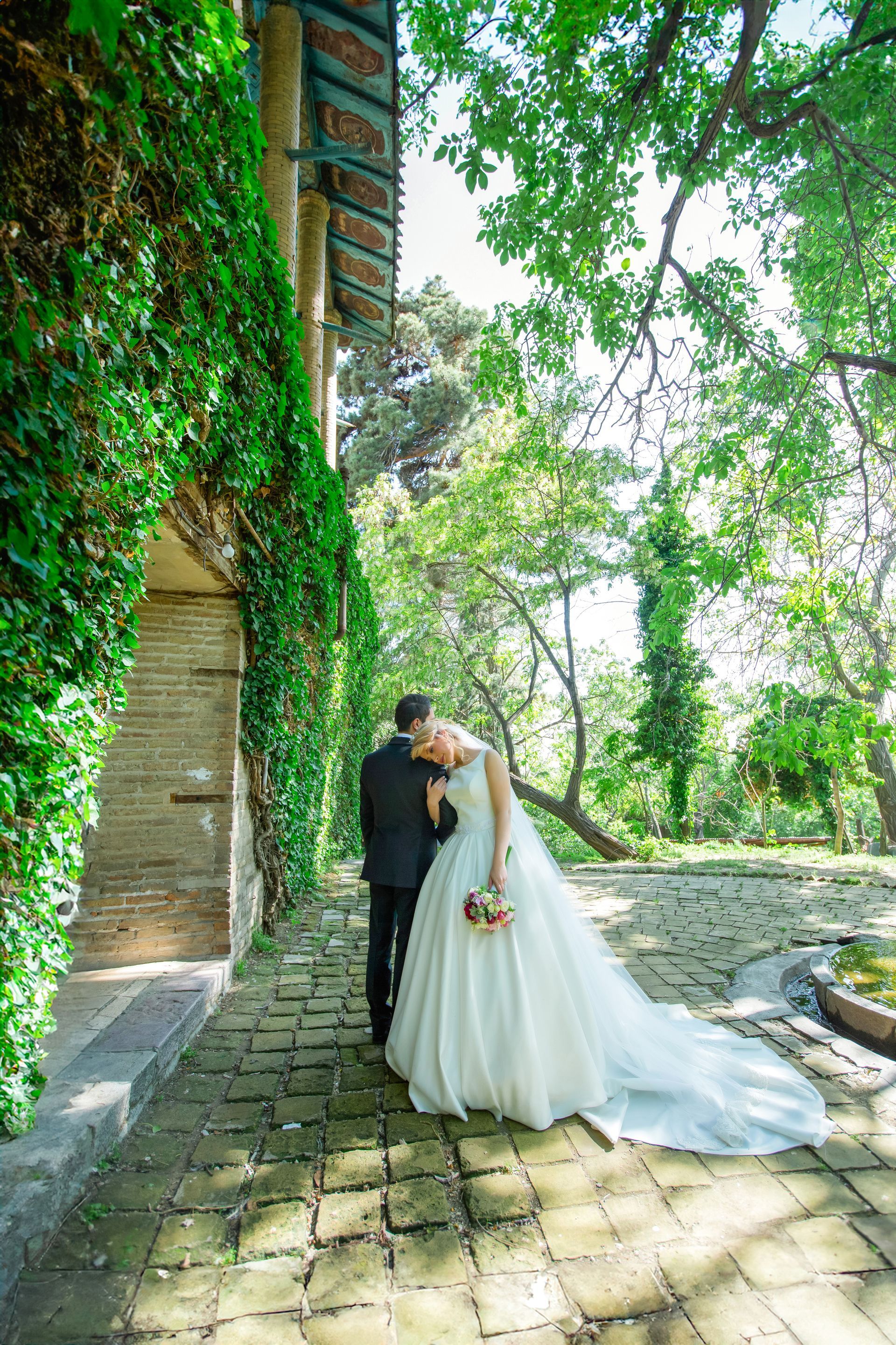 A bride and groom are kissing in front of a building covered in ivy.
