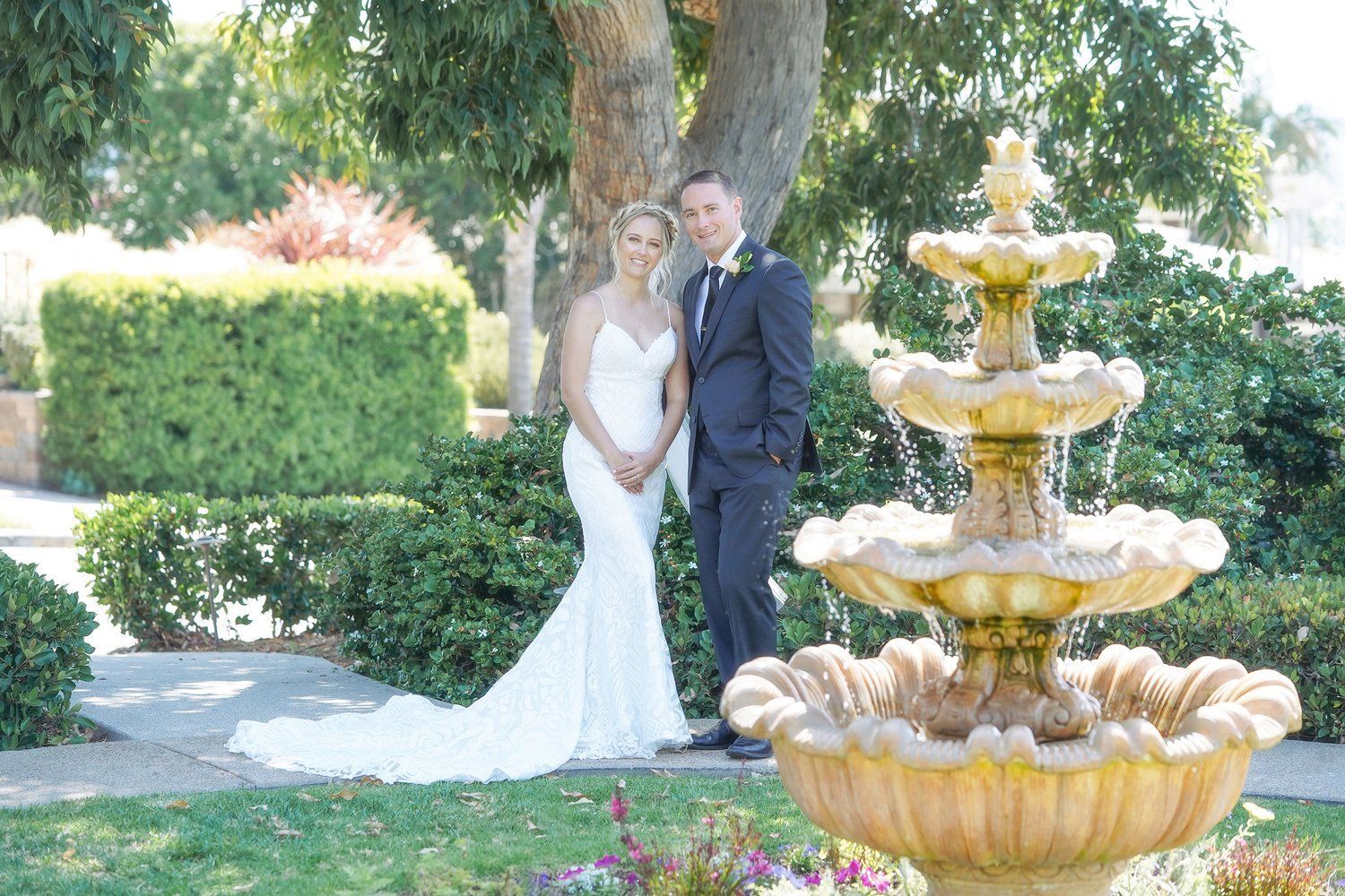 A bride and groom are posing for a picture in front of a fountain.