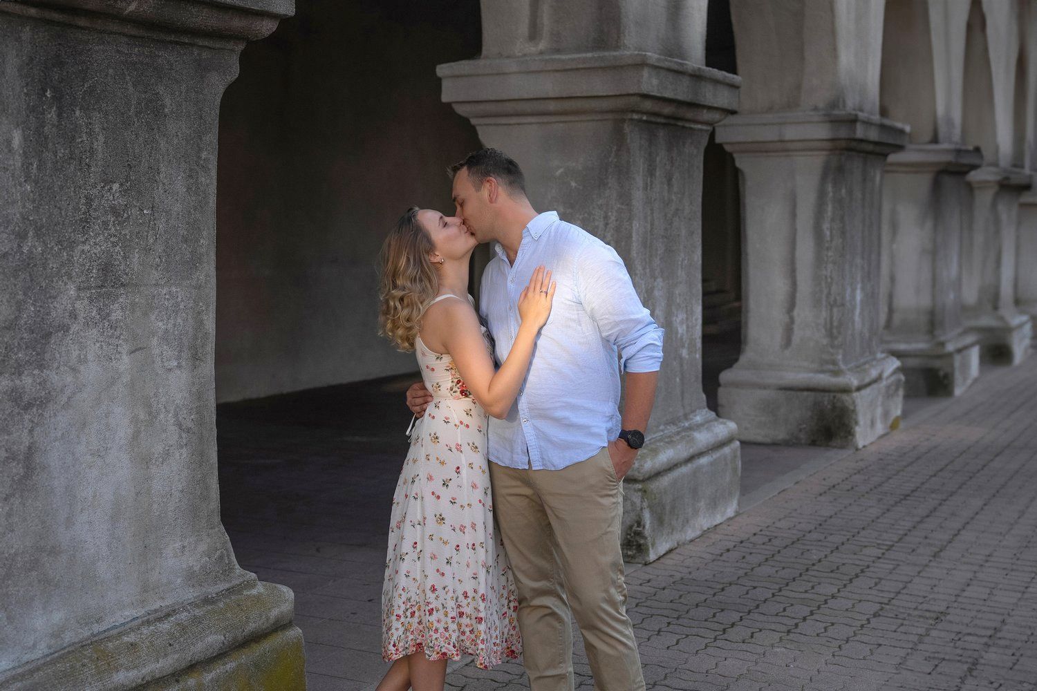 A man and a woman are kissing in front of a row of columns.
