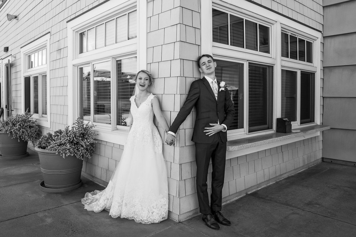 A bride and groom are standing next to each other in front of a building holding hands.