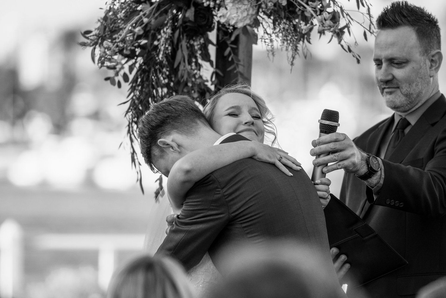A black and white photo of a bride and groom hugging during their wedding ceremony.