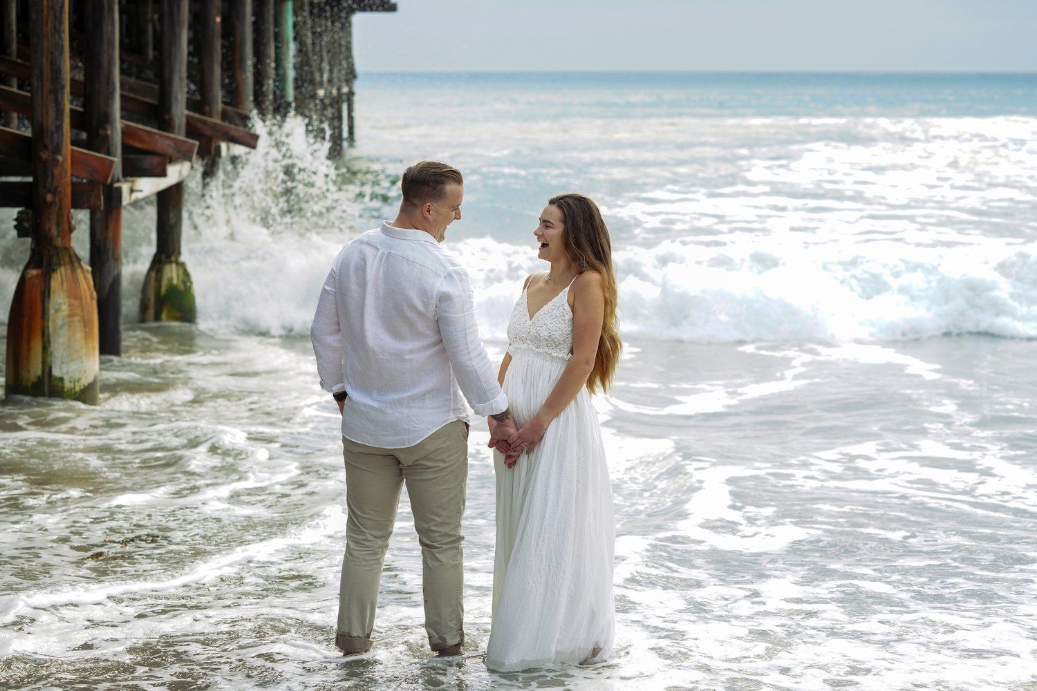A man and a woman are standing on the beach holding hands.