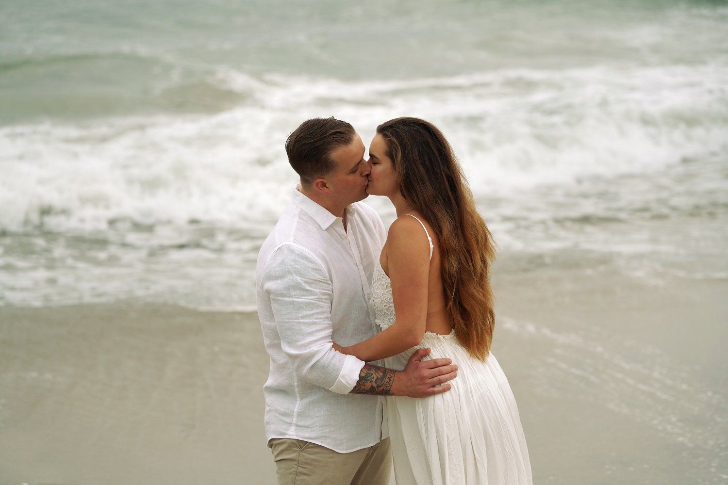 A man and a woman are kissing on the beach.