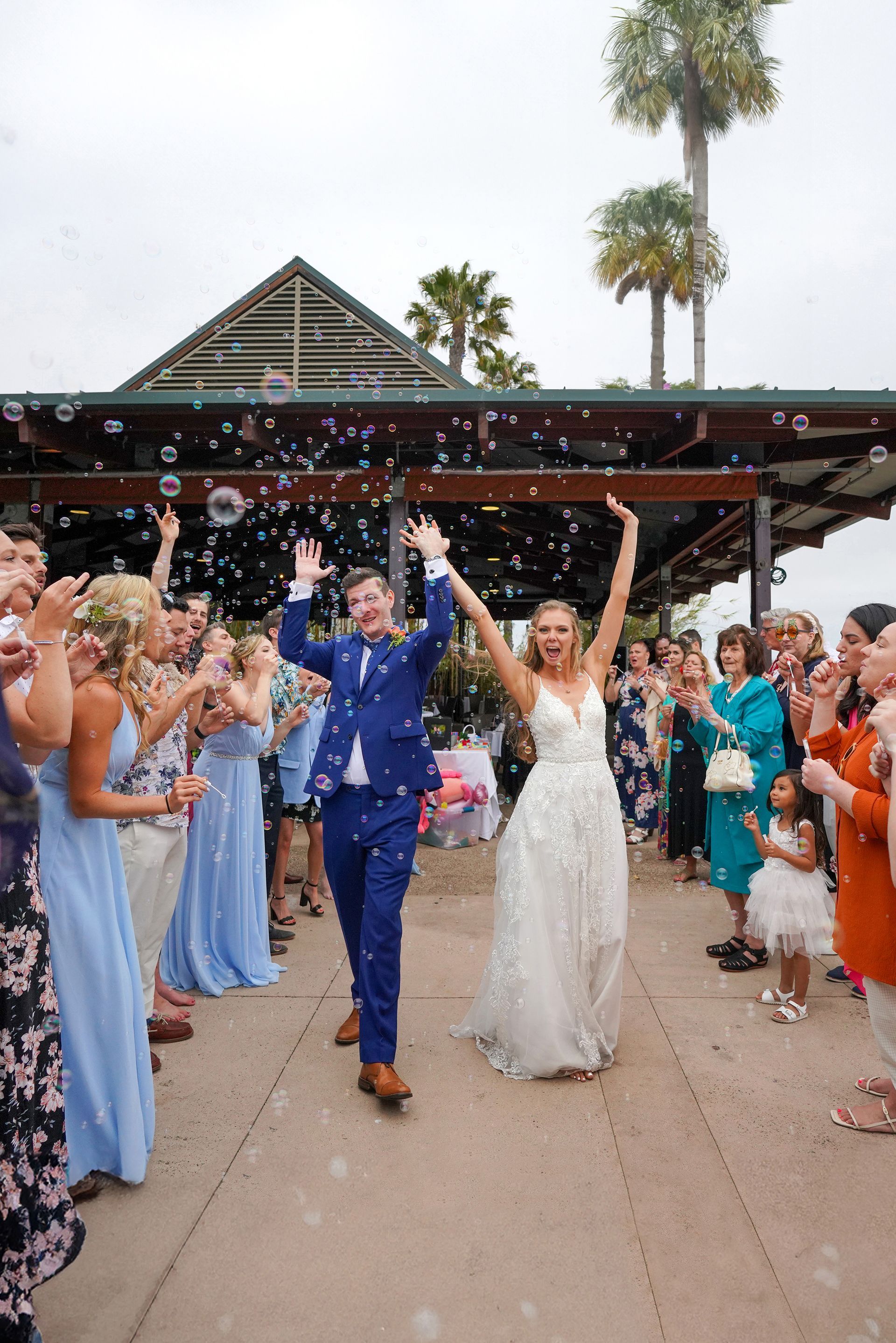 A bride and groom are walking through a crowd of people blowing soap bubbles.