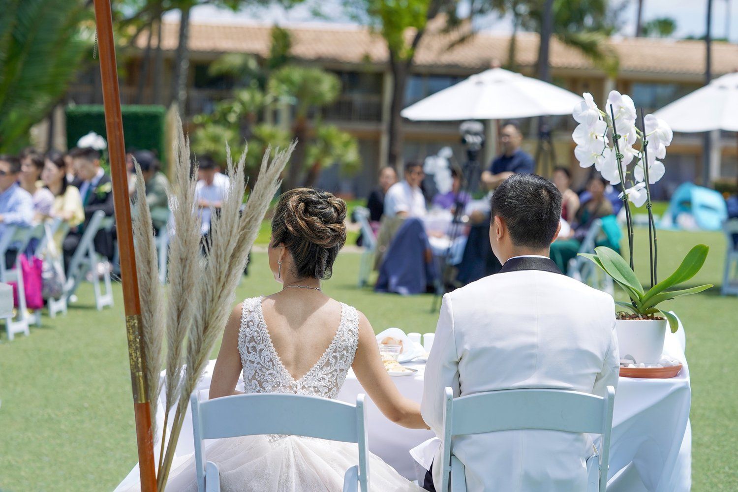 A bride and groom are sitting at a table holding hands at their wedding reception.