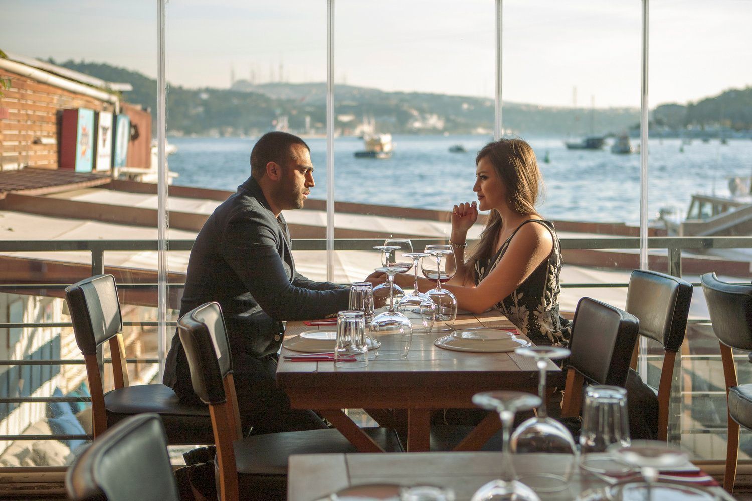 A man and a woman are sitting at a table in a restaurant with a view of the ocean.