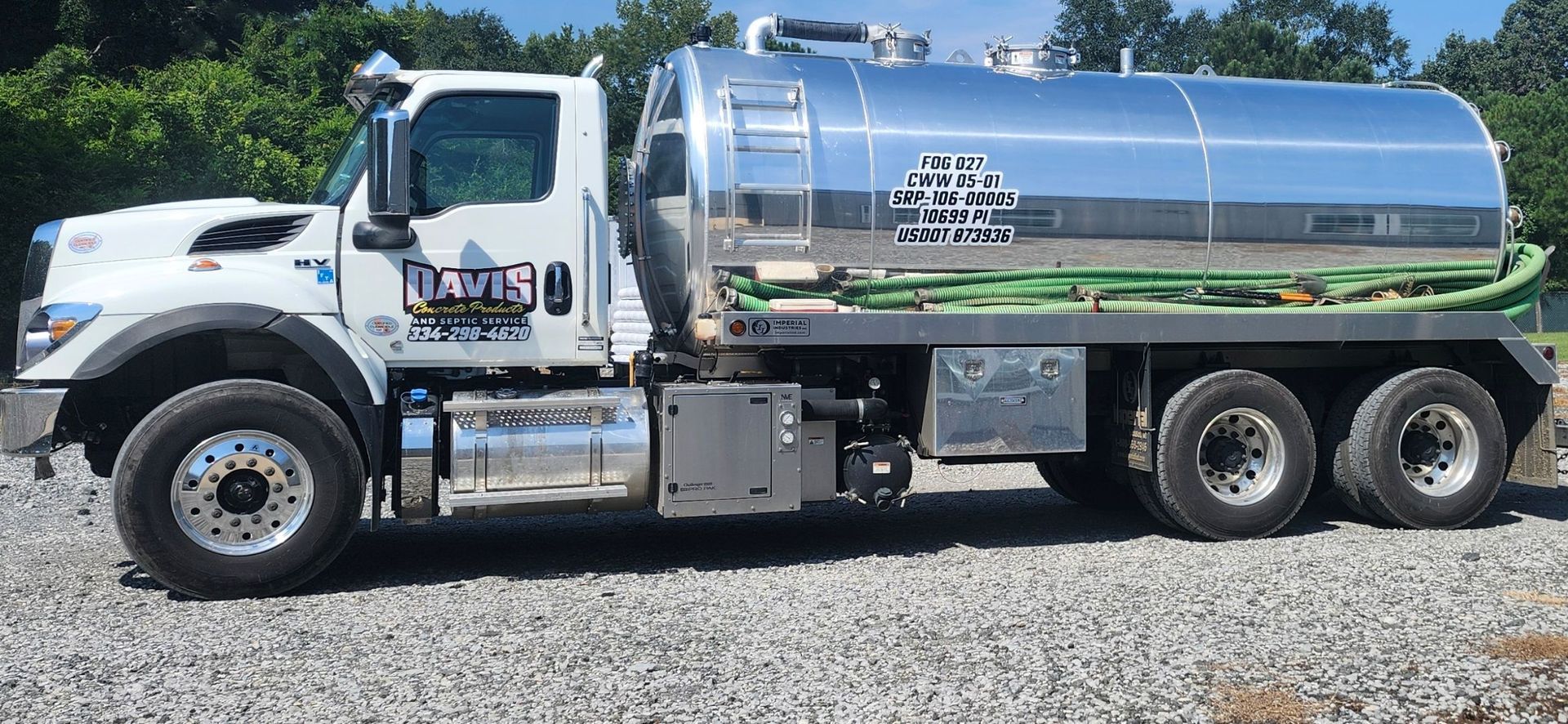 White septic service truck with a large, shiny tank parked on gravel.