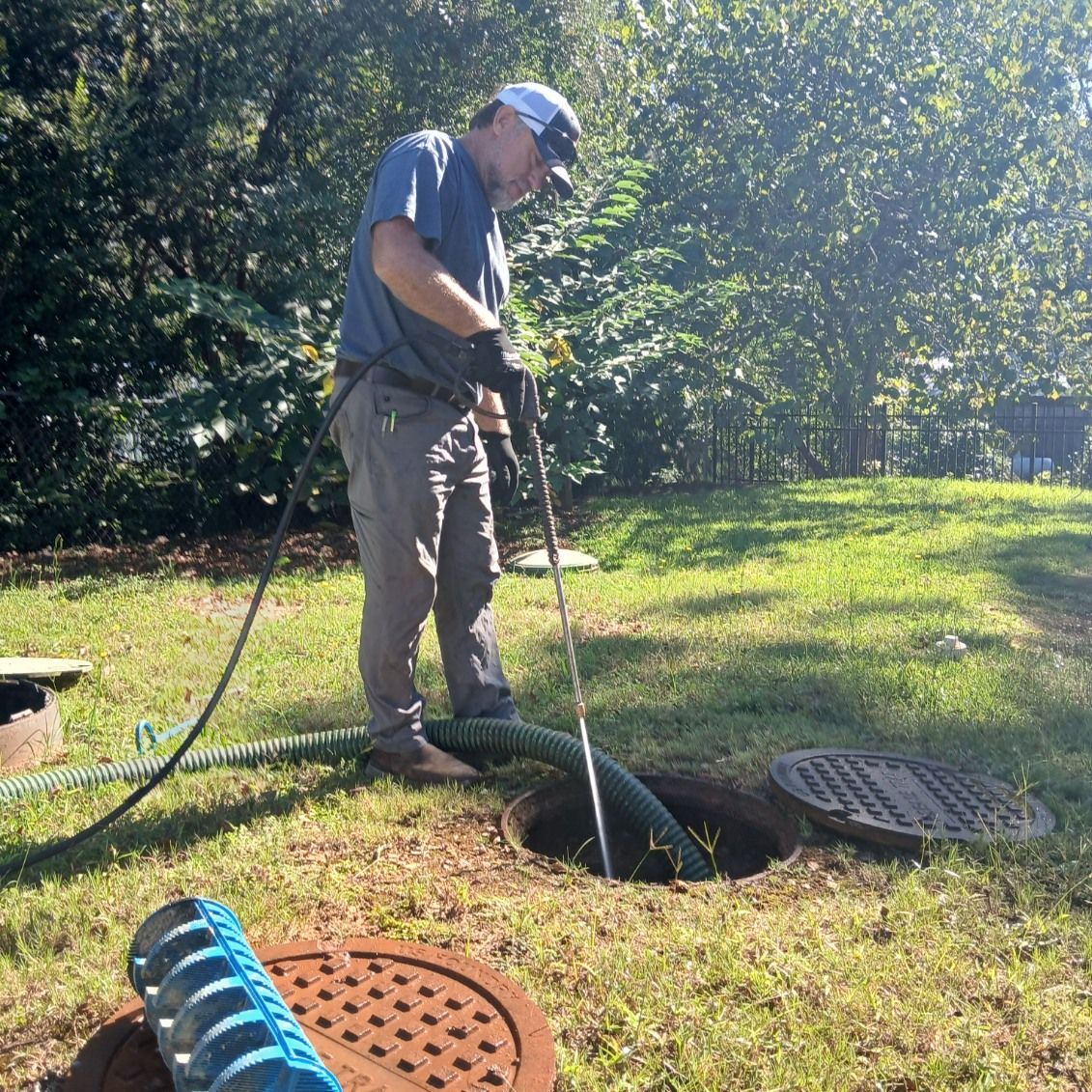 Man in a yard using a hose to clean a septic tank access point.