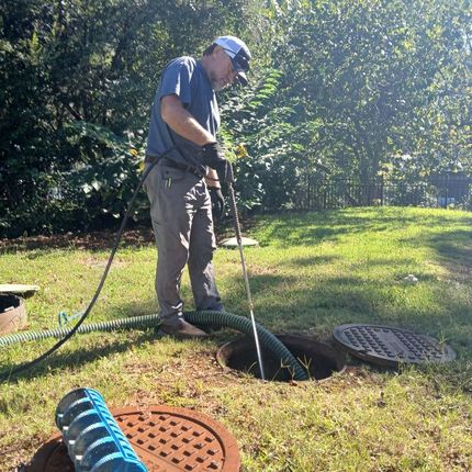 Man in a yard using a hose to clean a septic tank access point.