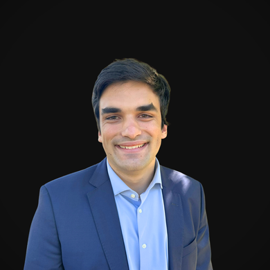 Man in a blue blazer and shirt smiling, against a black background.