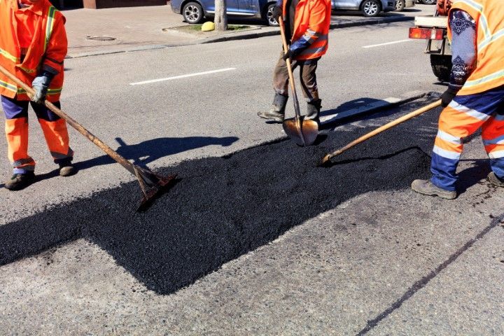 Workers smoothly out fresh asphalt on road