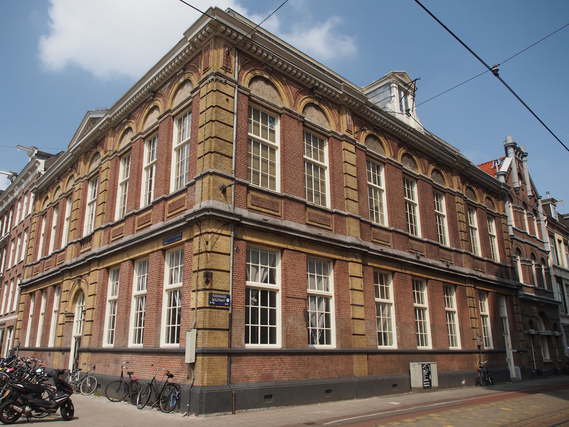 Een bakstenen gebouw op een straathoek met veel ramen en een klein uithangbord.