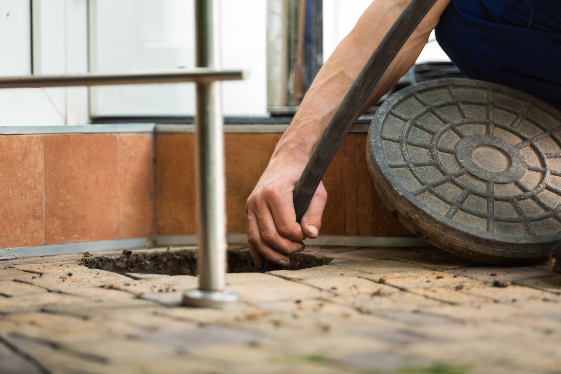 Hand pulling a drain cleaning hose from an open ground cleanout on a paved surface.