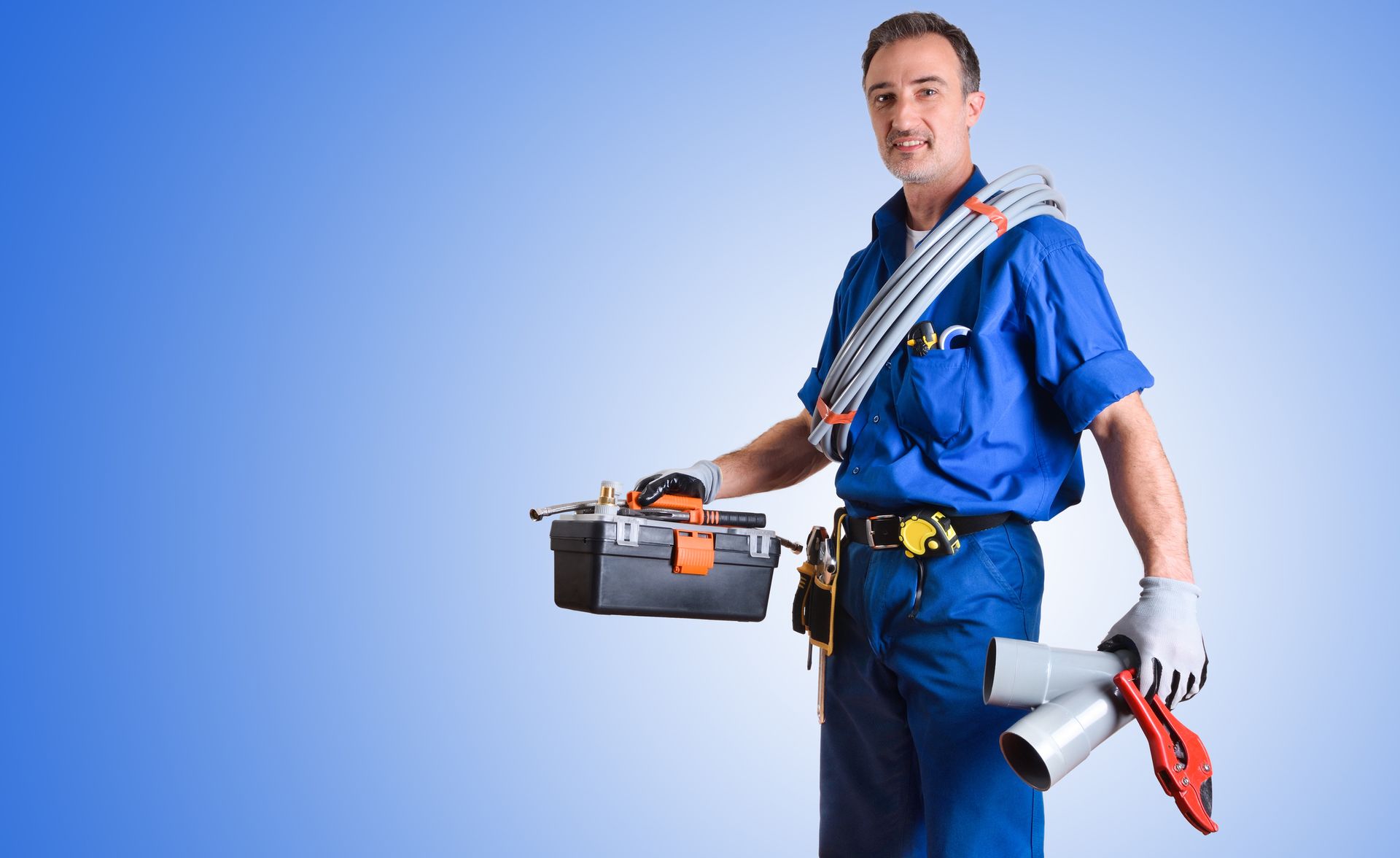 Portrait of a uniformed plumber with work tools in his hands and a blue gradient isolated background.