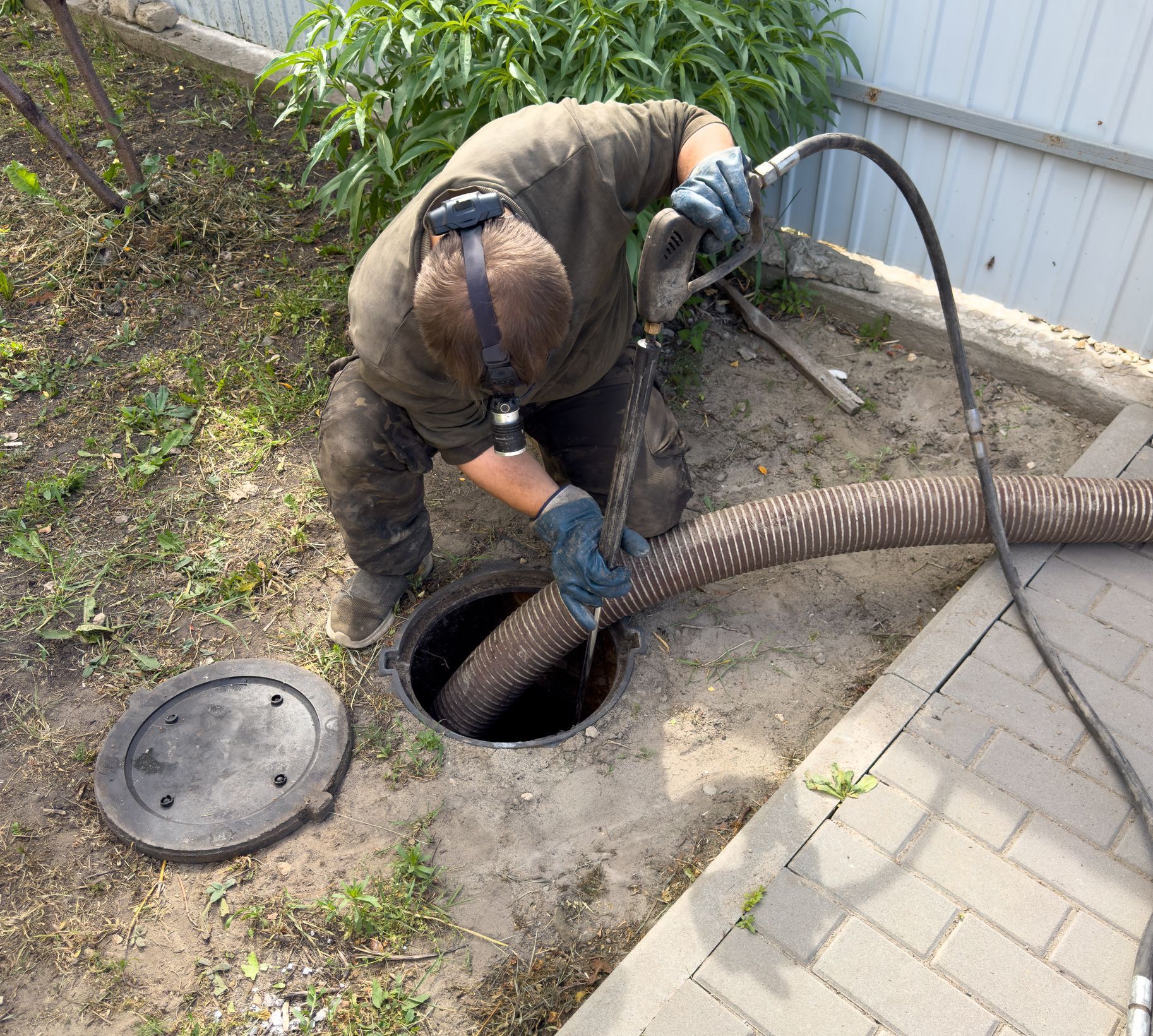 Drain cleaning technician using sewer vacuum hose to unclog underground septic access line service.