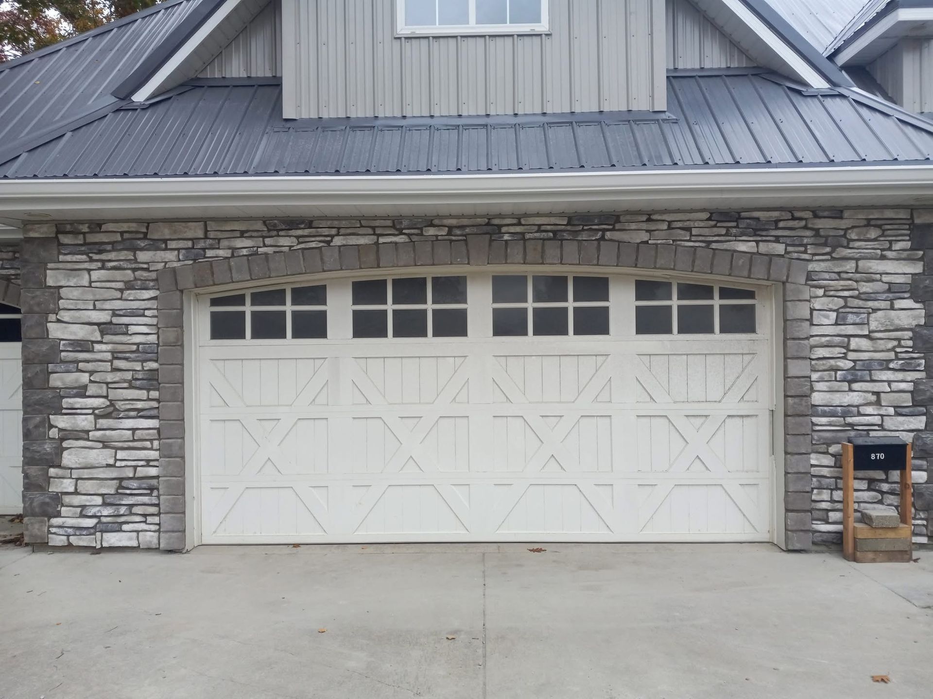 White garage door with stone facade, arched top, beneath gray roof.