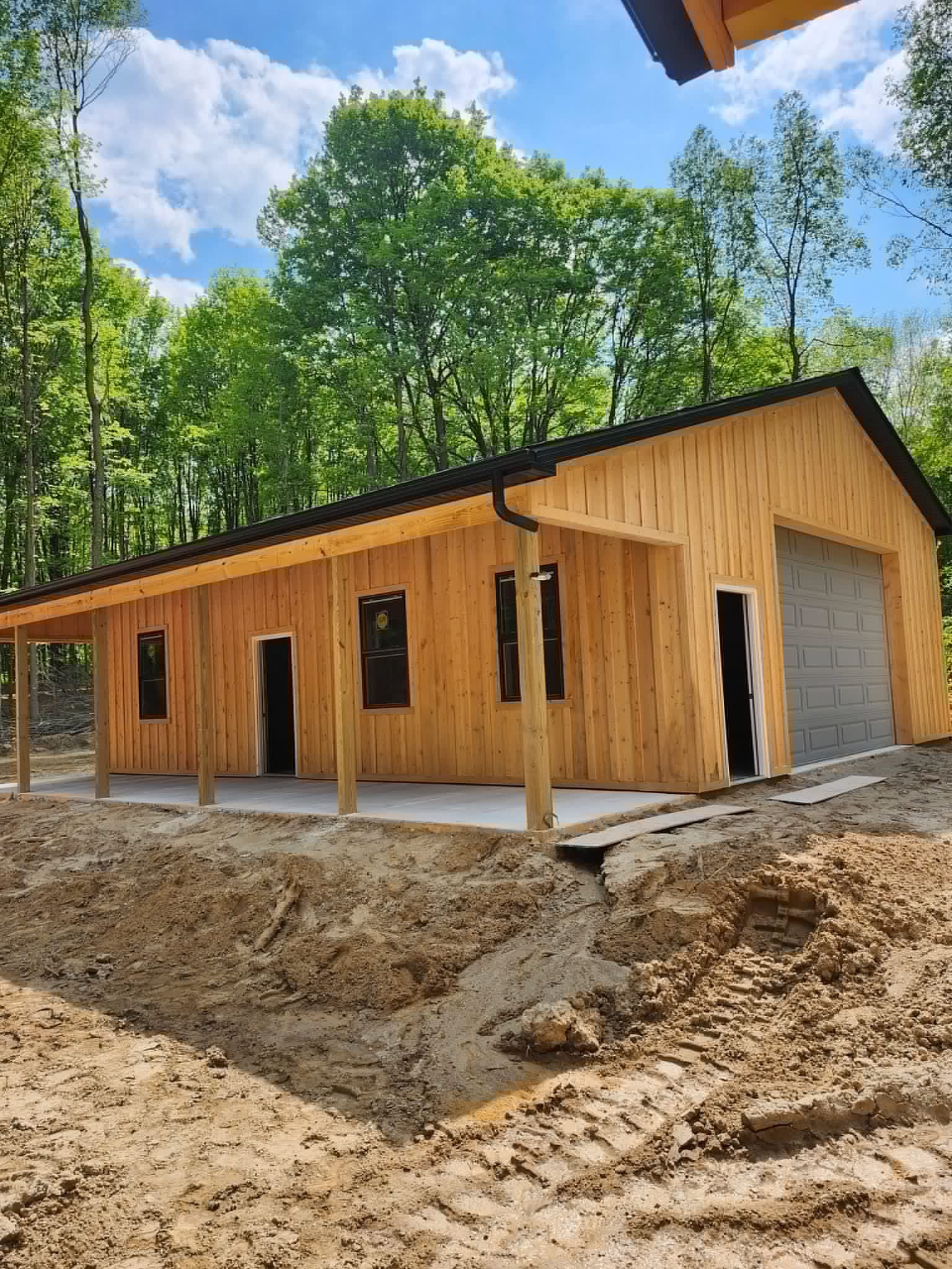Wooden building with a concrete foundation, in a wooded area. The garage door is open.