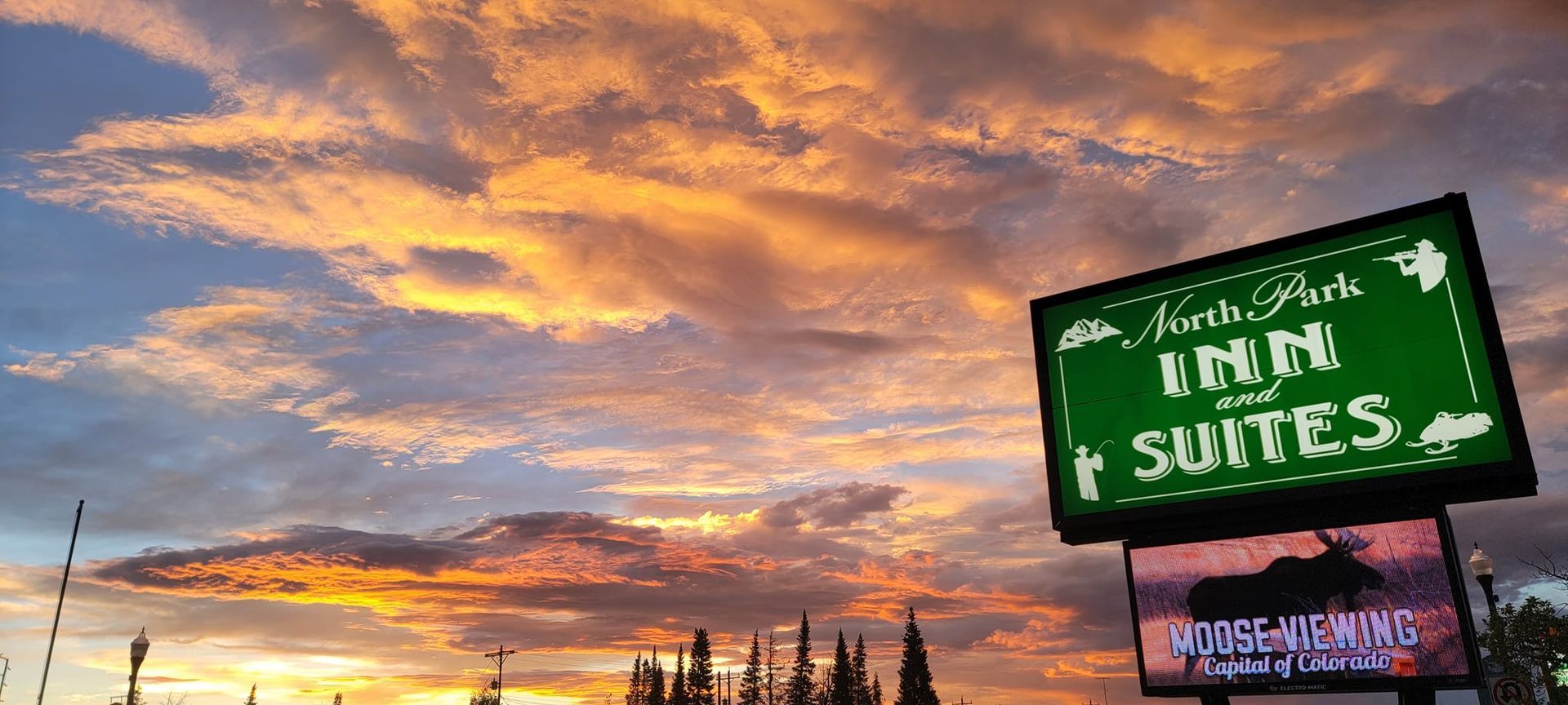 Sunset sky behind a green sign for North Park Inn and Suites. Below is a sign with a moose on it.