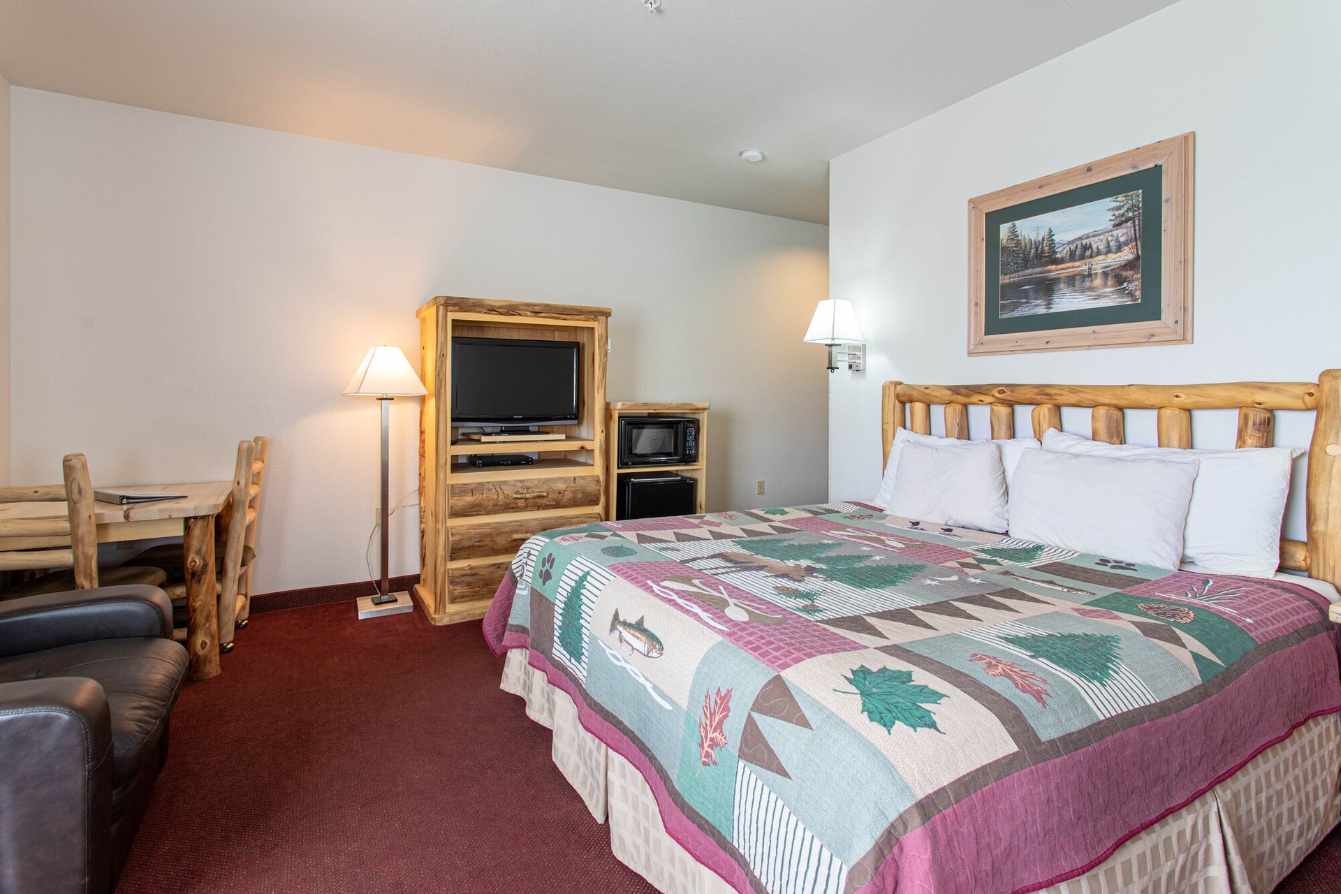 Rustic hotel room with a bed, wooden furniture, TV, and a nature-themed quilt.