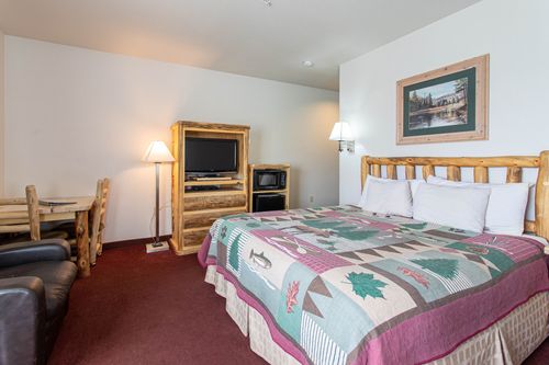 A hotel room with a king size bed , television , table and chairs.