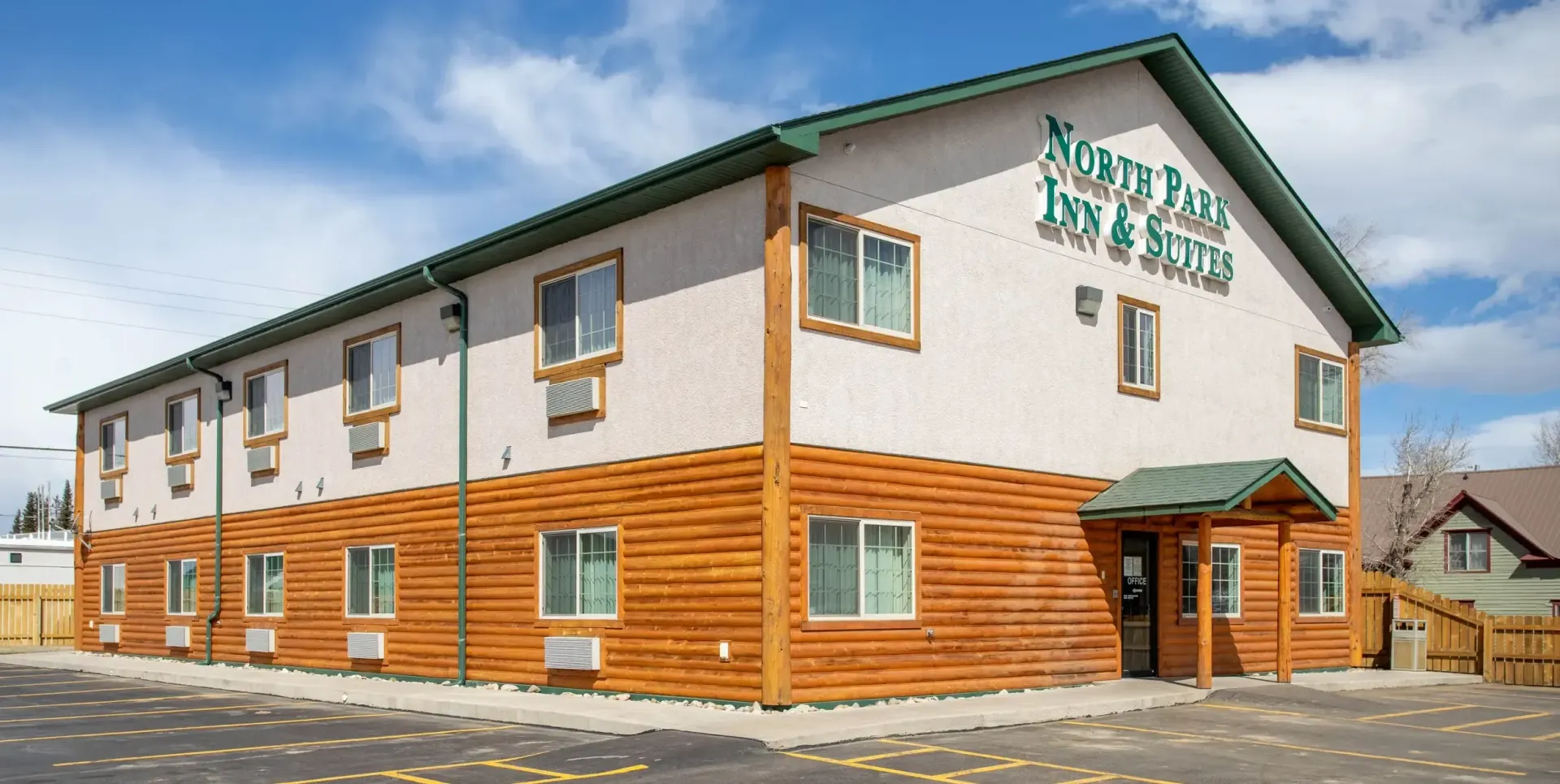 Two-story hotel with light-colored upper facade and wood paneling on the bottom, under a blue sky.