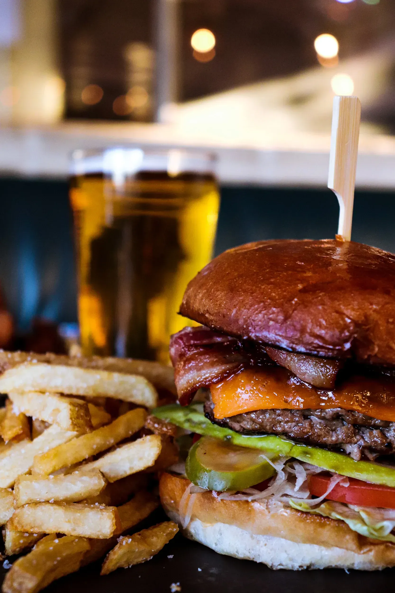 Burger with fries and beer, featuring bacon, cheese, and fixings on a toasted bun.
