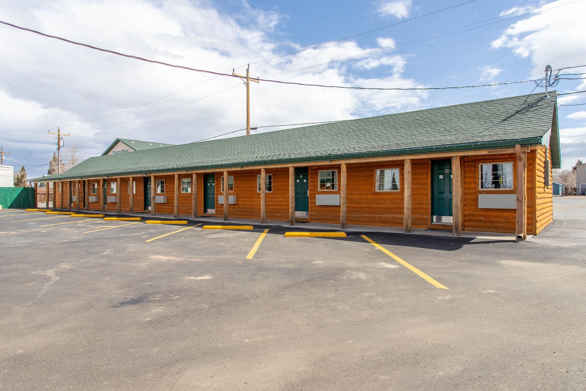 Motel with brown log siding, green roof, and parking spaces under a partly cloudy sky.