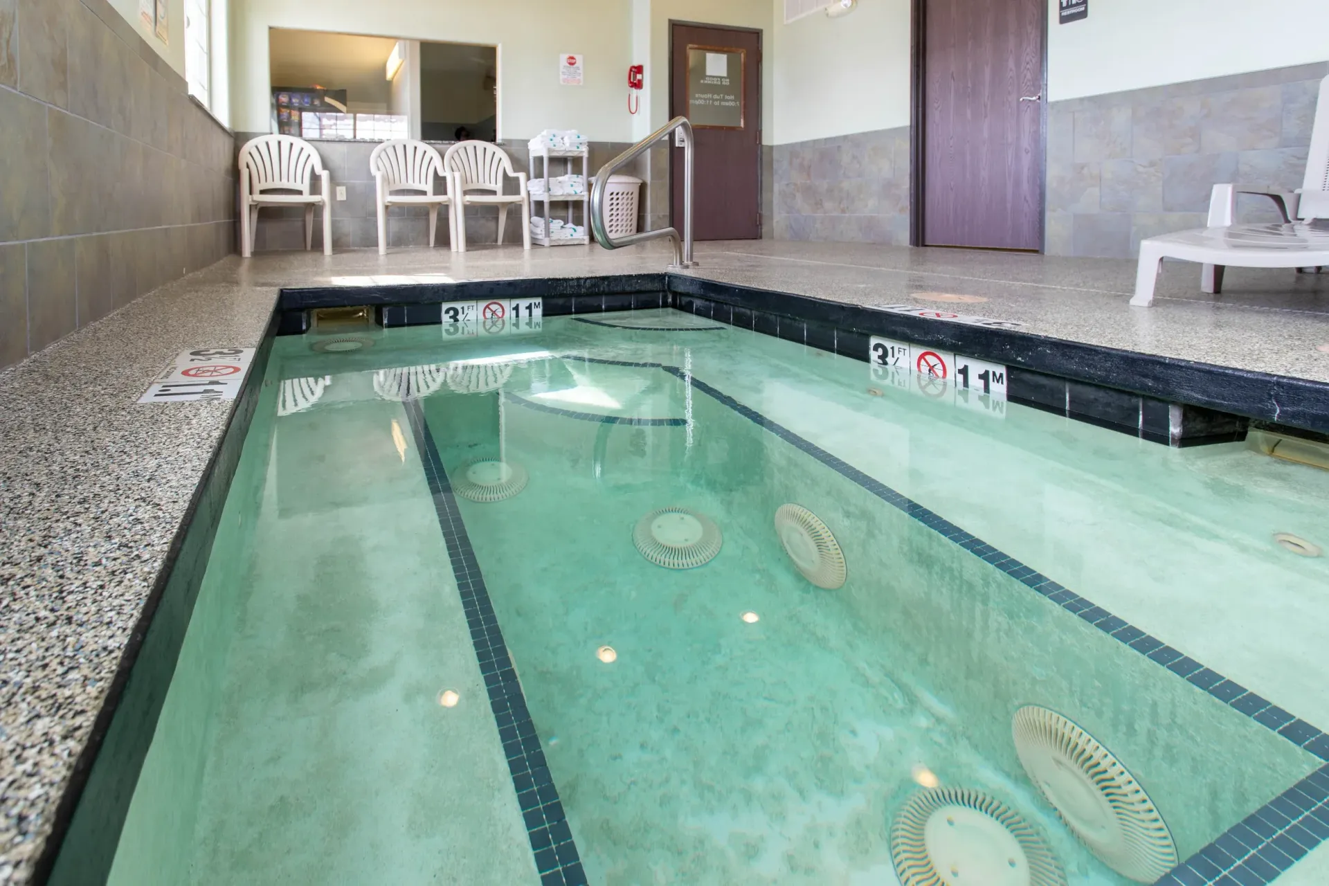 Indoor therapy pool with benches, chairs, and a door.