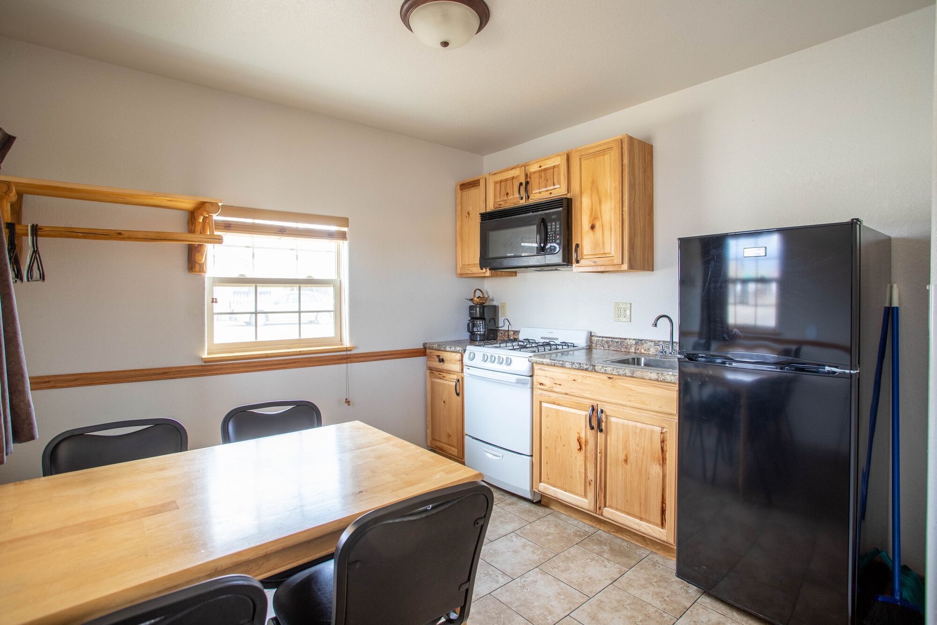 Small kitchen with table, chairs, and appliances: black fridge, microwave, and white stove.