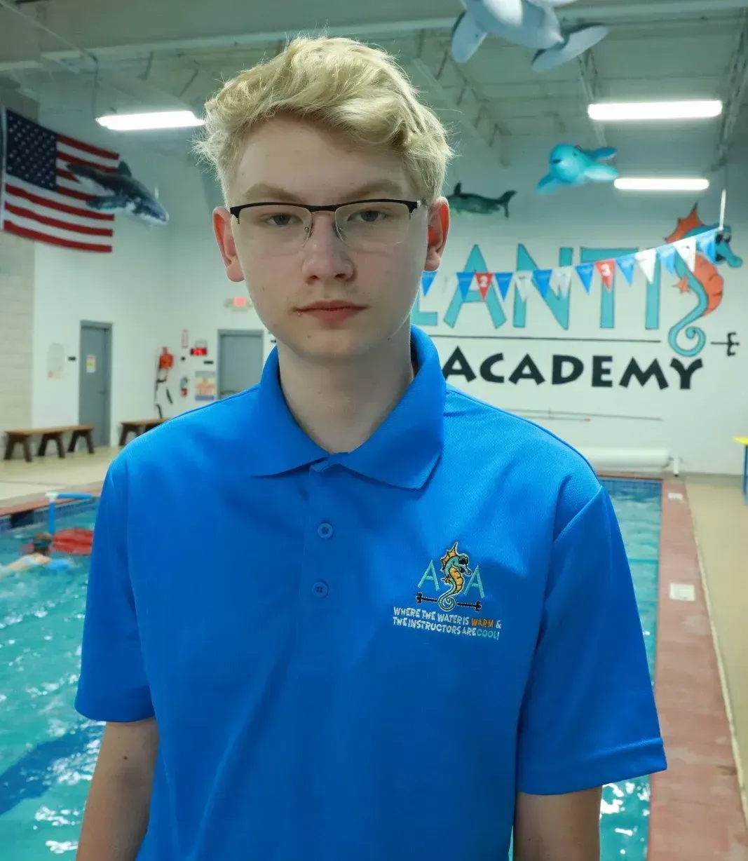 Teenager wearing glasses and a blue polo shirt standing by a pool in front of a wall with