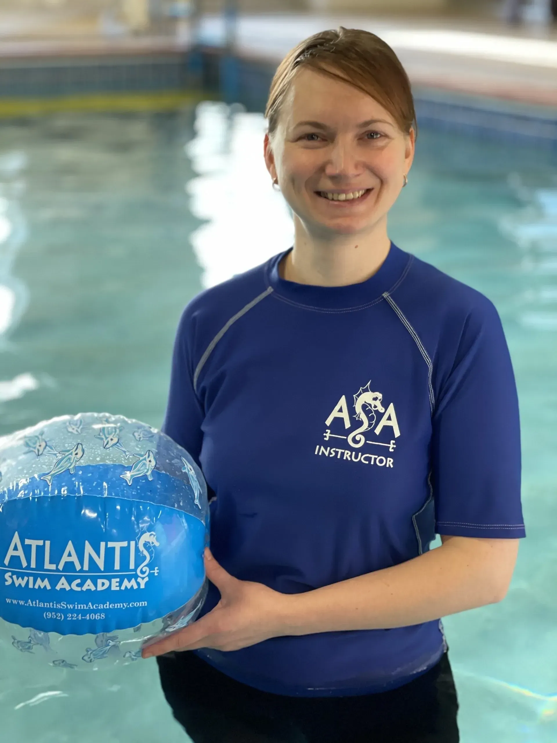 Woman in blue ASA instructor shirt holding a beach ball in a pool.