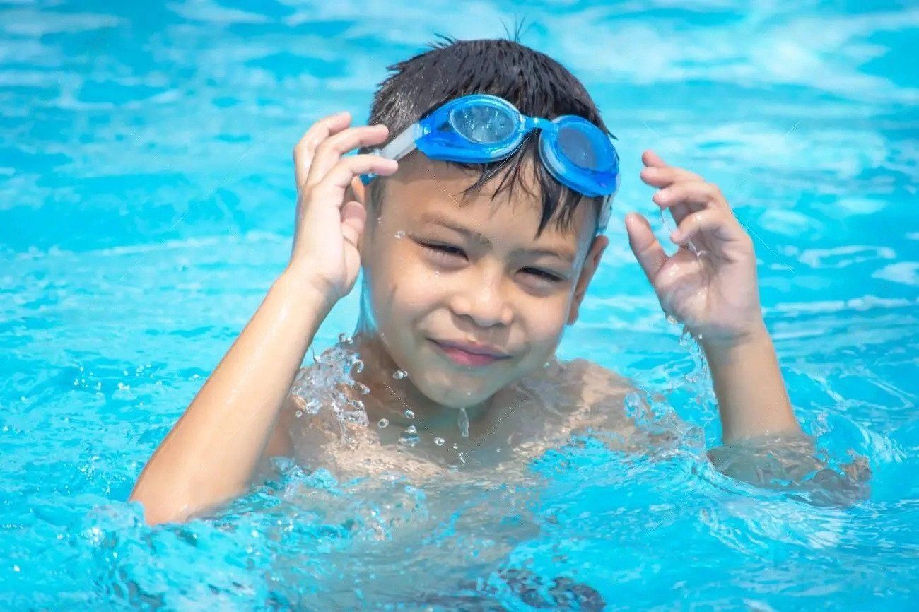A parent helping a child put on goggles at the pool side