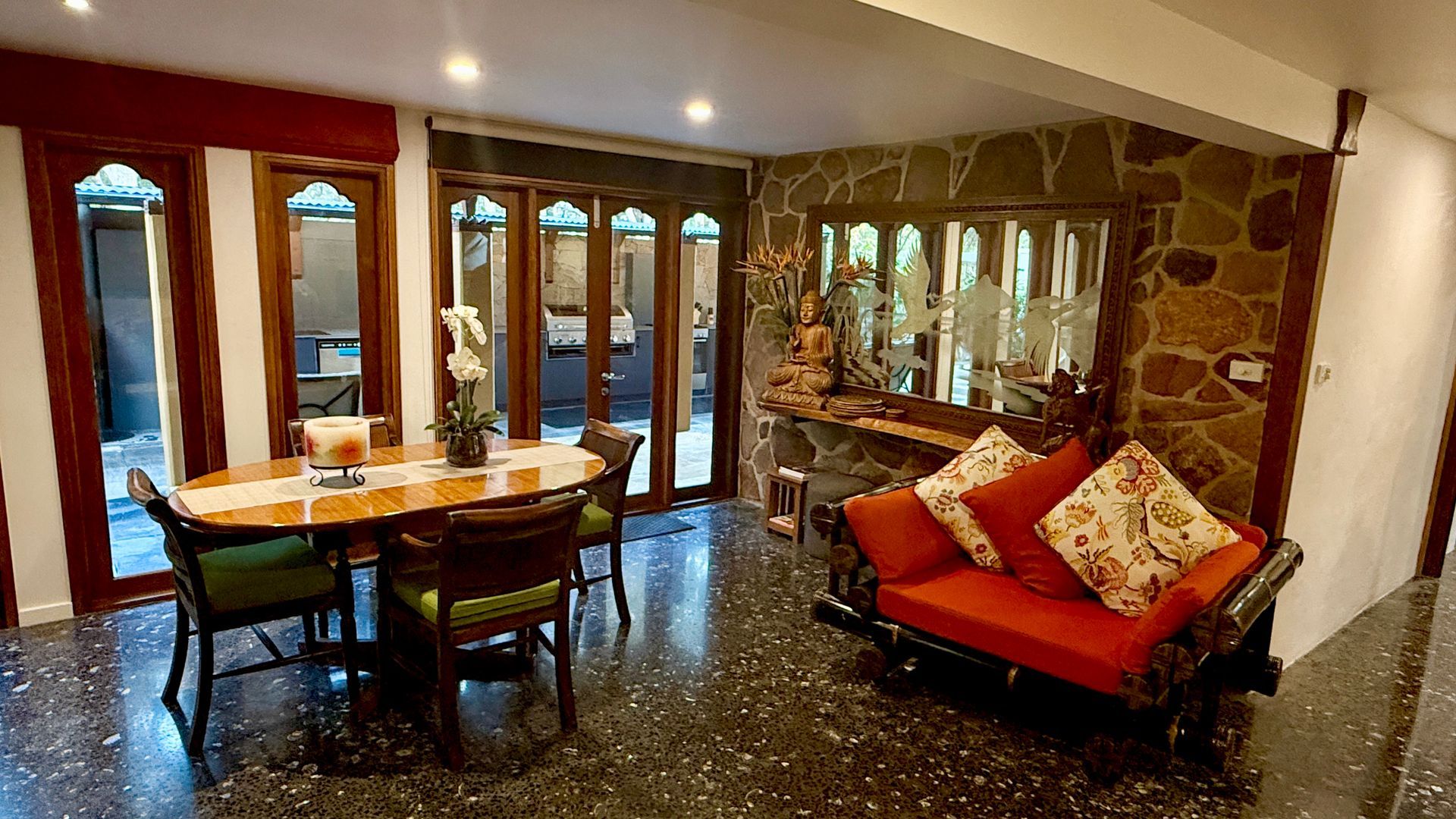 Dining room with a table, chairs, and a sofa against a stone wall — Bali at the Bay in Nelson Bay, NSW