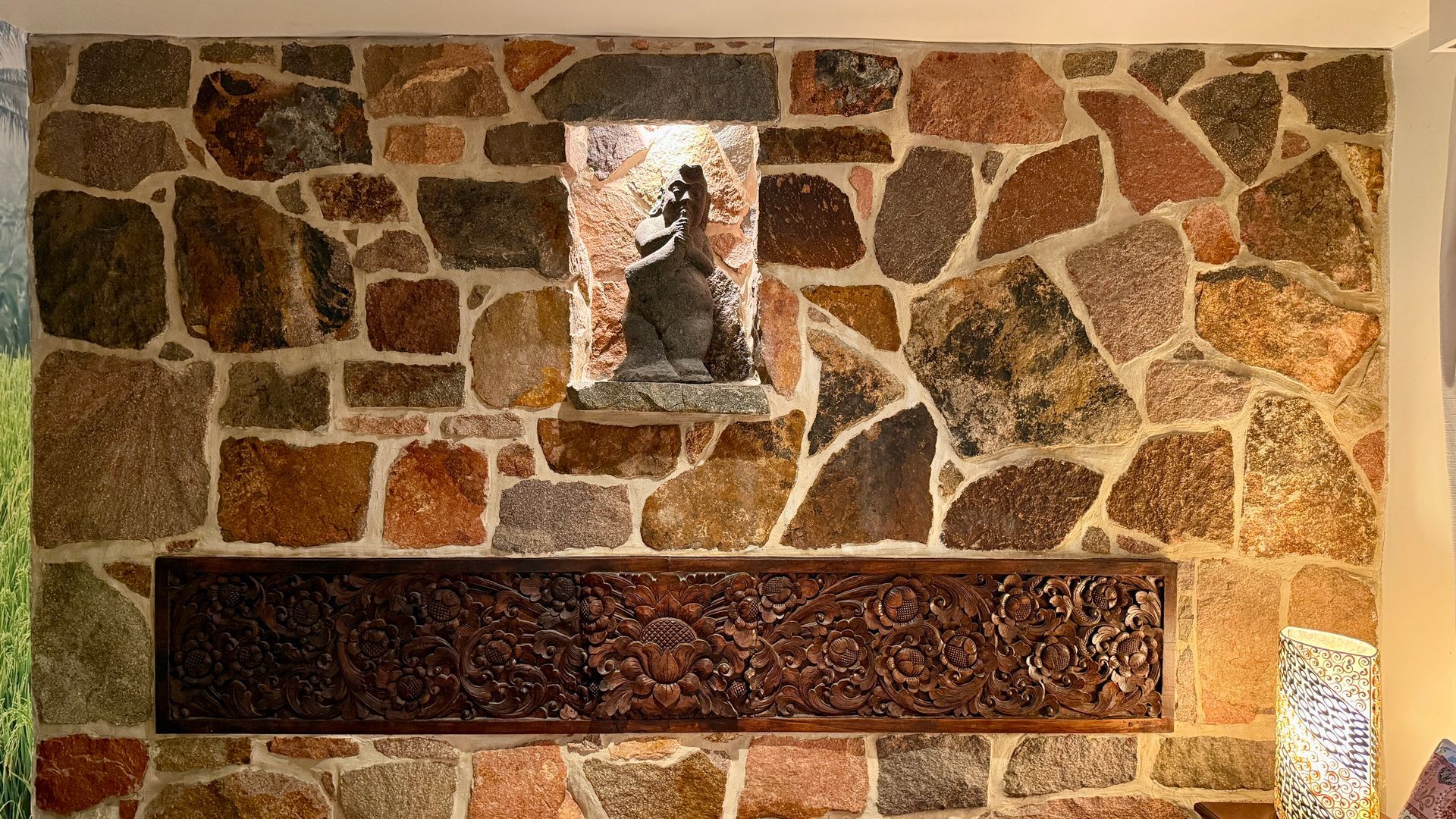 Stone wall with a carved wooden panel and a statue in a niche — Bali at the Bay in Nelson Bay, NSW