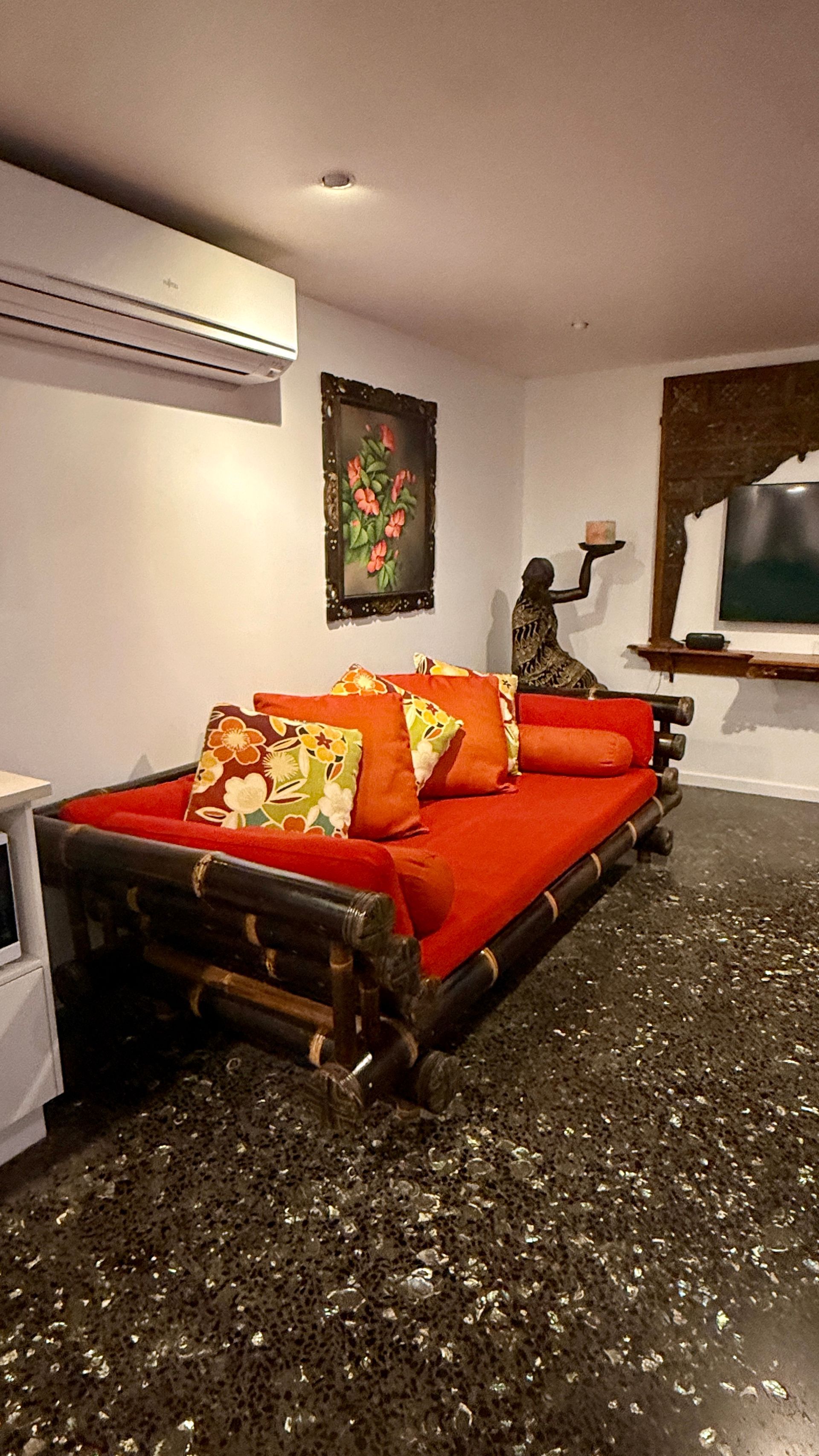 A cozy room with a bamboo daybed, orange cushions, a framed painting, and a statue — Bali at the Bay in Nelson Bay, NSW