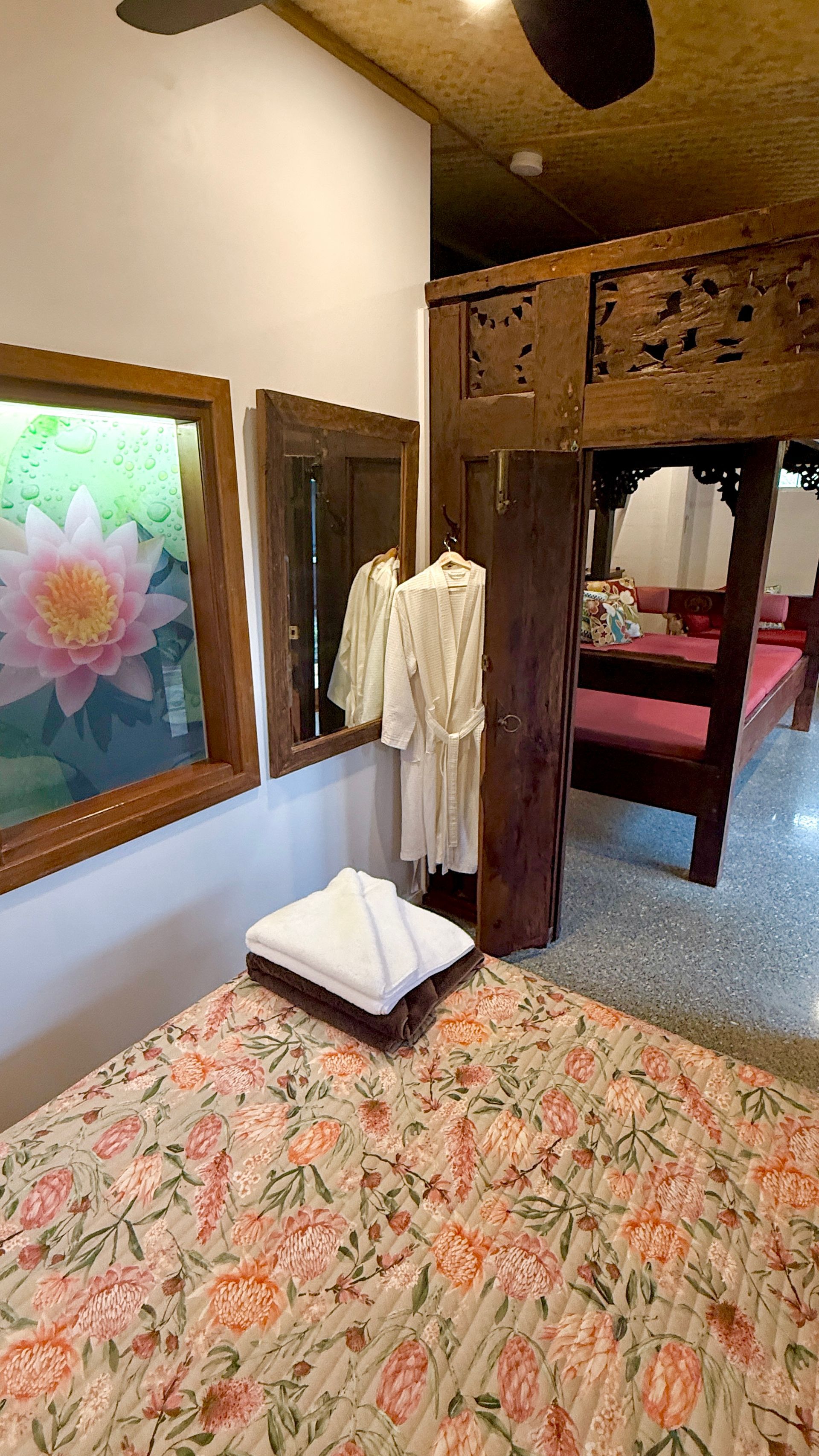 Bedroom with carved wood, floral bedding, and a mirror reflecting a bathrobe.