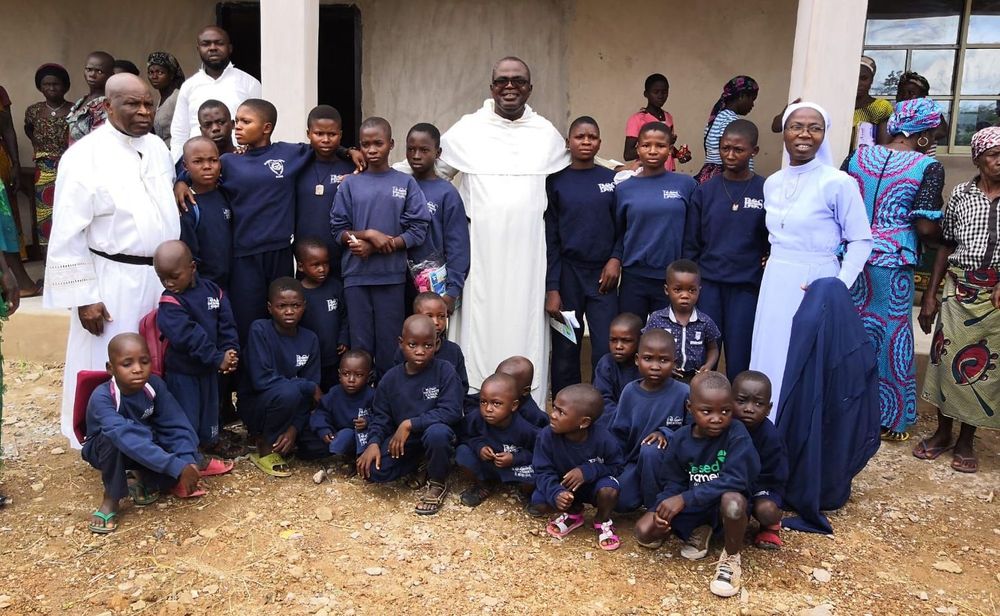 Nigerian school children standing around a Nigerian priest and nun and other clergy and local adults.