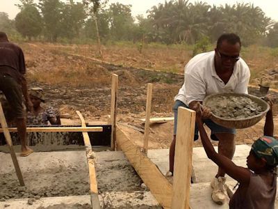 Men and women building the foundation of the school, passing buckets and assembling wooden boards