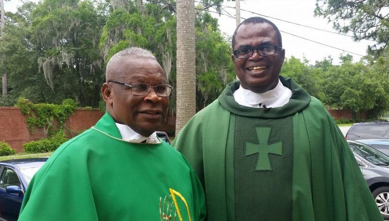 Two Nigerian priests smiling next to one another in green robes