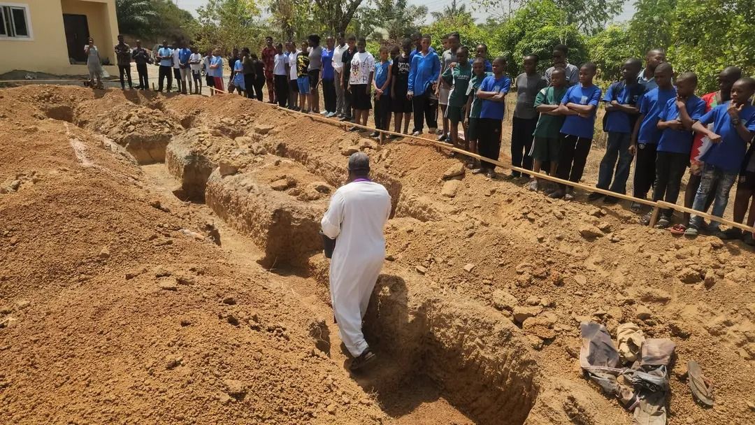 priest walking through the dug foundation and surrounded by community members