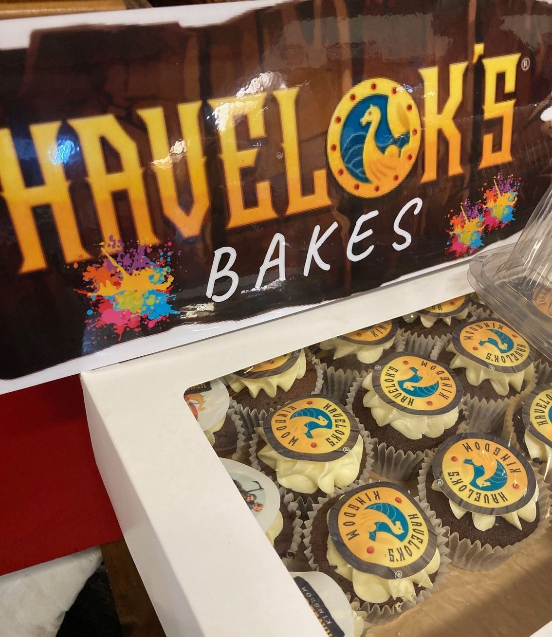 A box of cupcakes under a sign that says havelok 's bakes