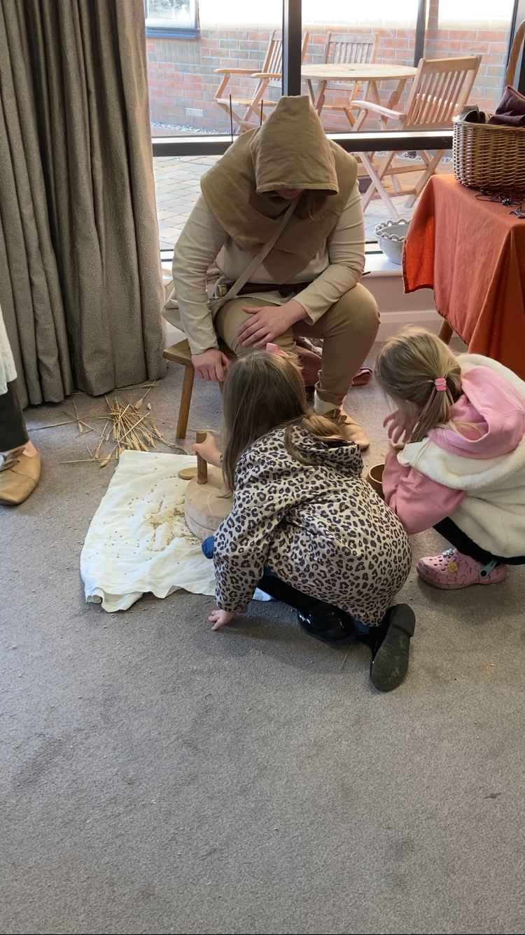 A man in a hooded robe is kneeling down next to two little girls.