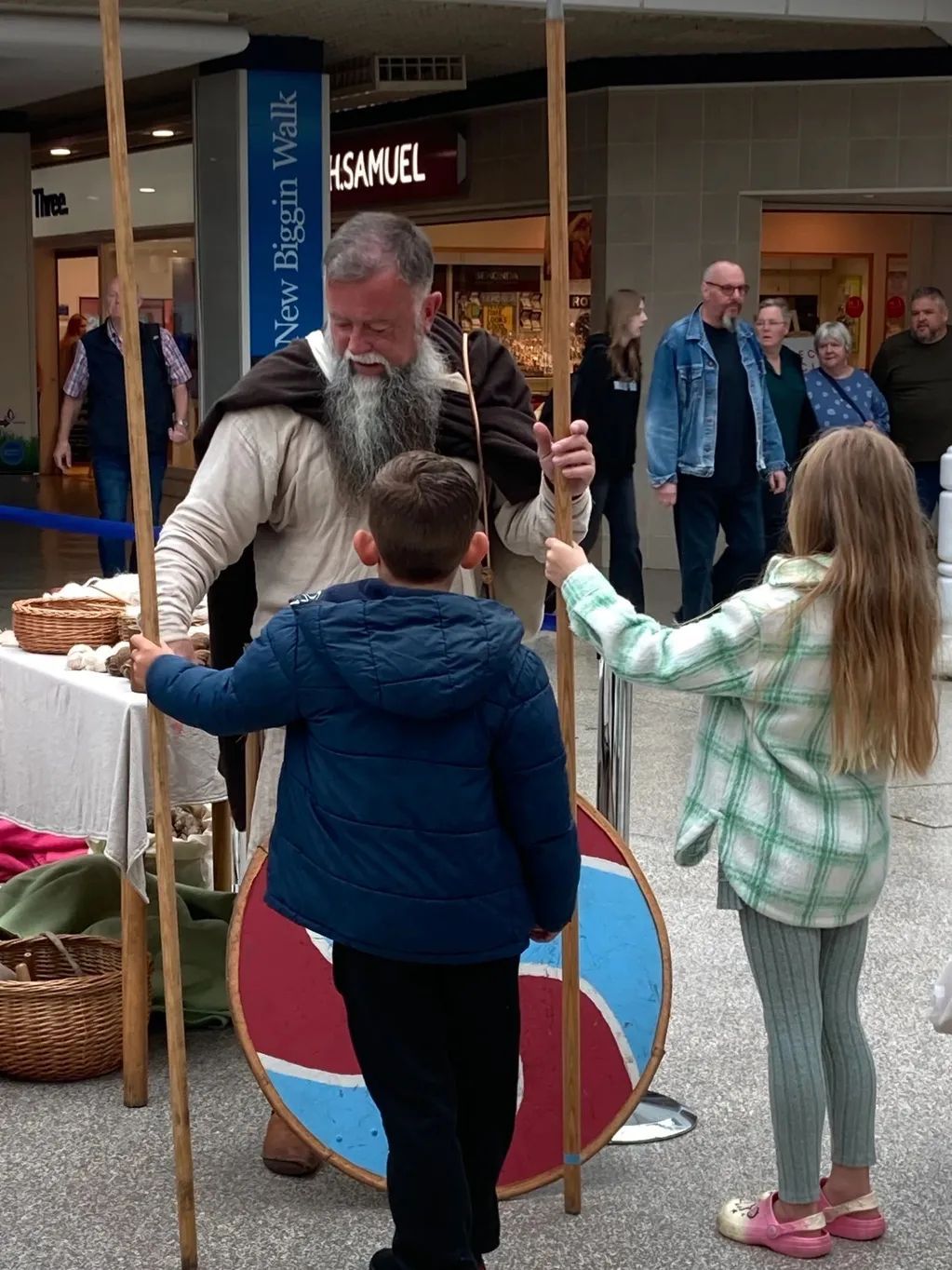 A man with a beard is standing next to a boy and a girl holding a shield.