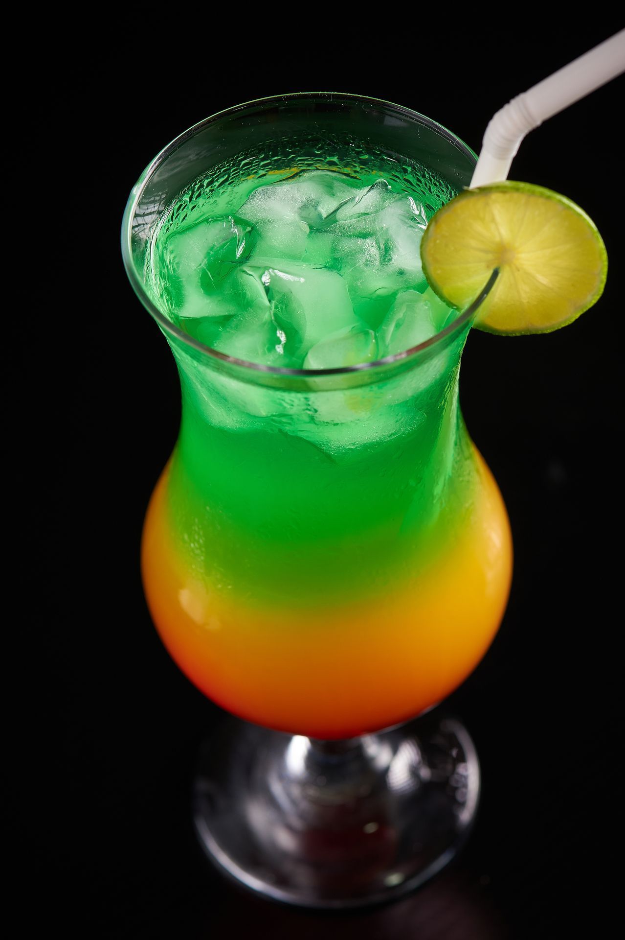 Un primer plano de un cóctel colorido en un vaso con hielo y una pajita.