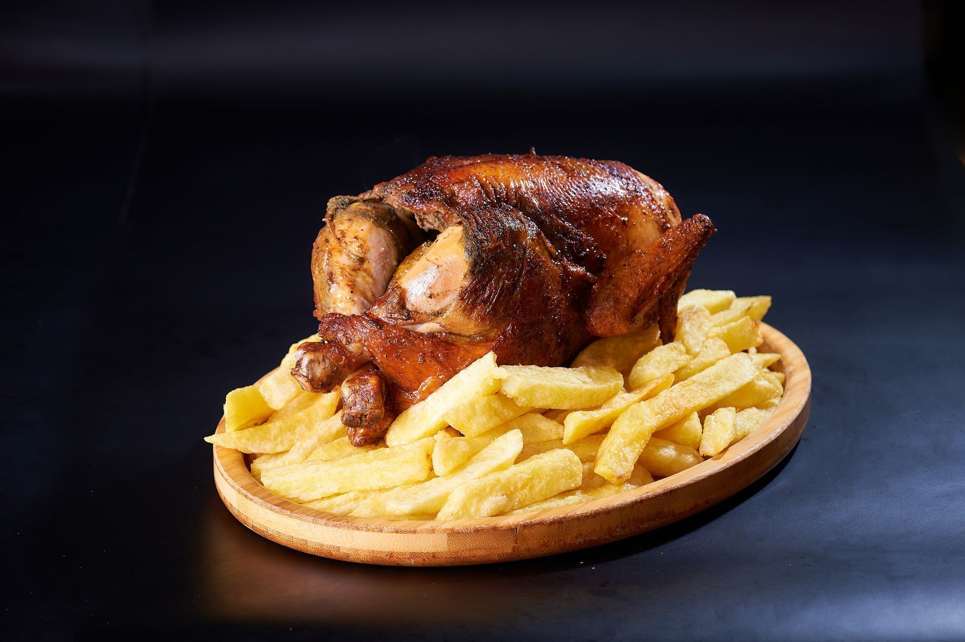 Un pollo asado y patatas fritas en un plato de madera.